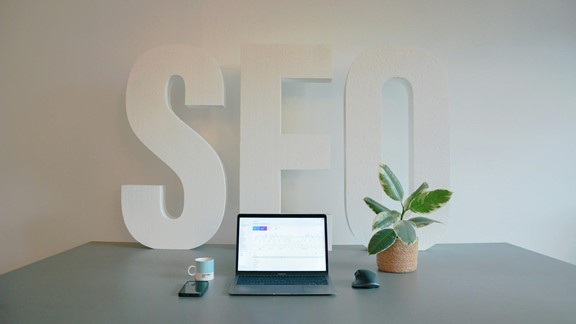 Large SEO letters on a desk beside an open laptop showing an analytics dashboard
